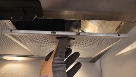 Une main gantée enlève le filtre métallique d'une hotte aspirante